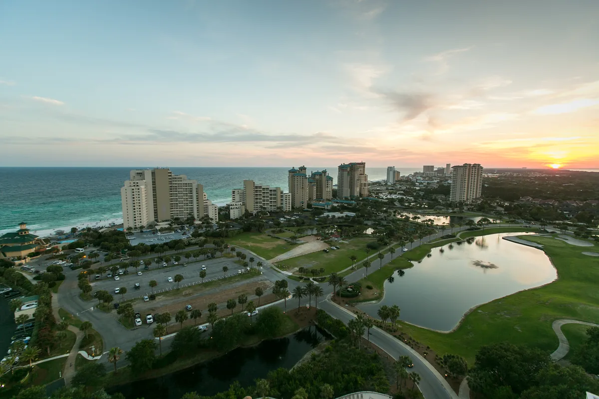 Aerial view of Destin at sunset, tall beachfront condominium towers along the Gulf shoreline with a coastal lake in the foreground